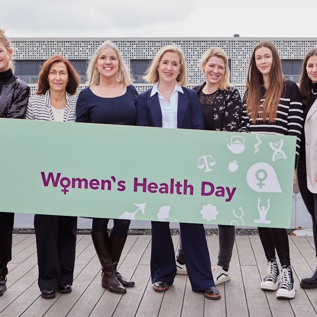 Sechs Frauen halten gemeinsam ein waagerechtes Plakat mit dem Slogan „Women's Health Day“.