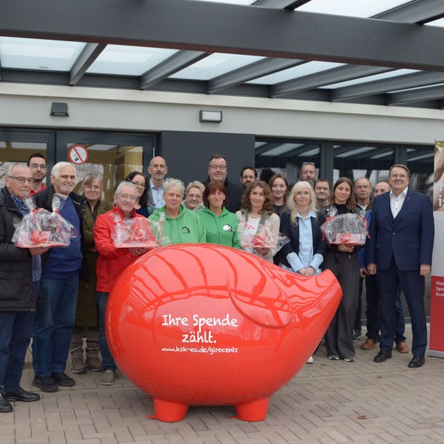 Vertreter von Vereinen und Kreissparkasse stehen für ein Gruppenfoto hinter einem überdimensionalen roten Sparschwein mit der Aufschrift „Ihre Spende zählt“.