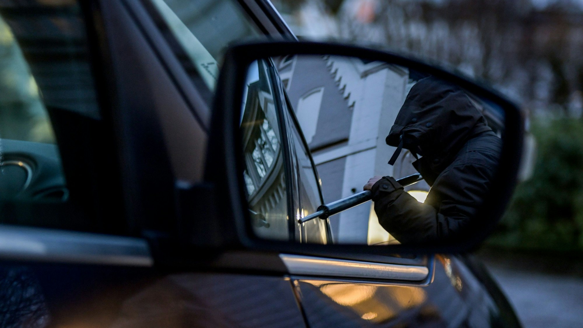 Ein Mann versucht, eine Autotür mit einer Metallstange aufzubrechen (gestellte Szene).