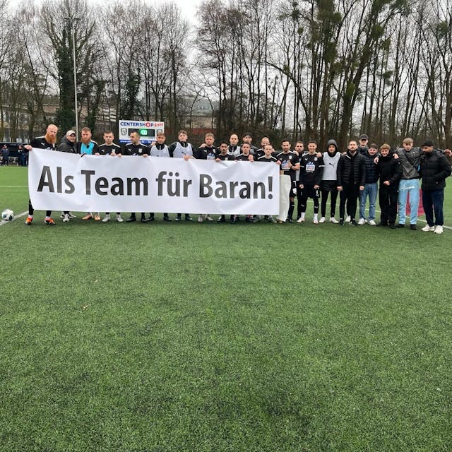 Die Spieler des SSV Jan Wellem halten ein Banner mit der Aufschrift "Als Team für Baran!" hoch