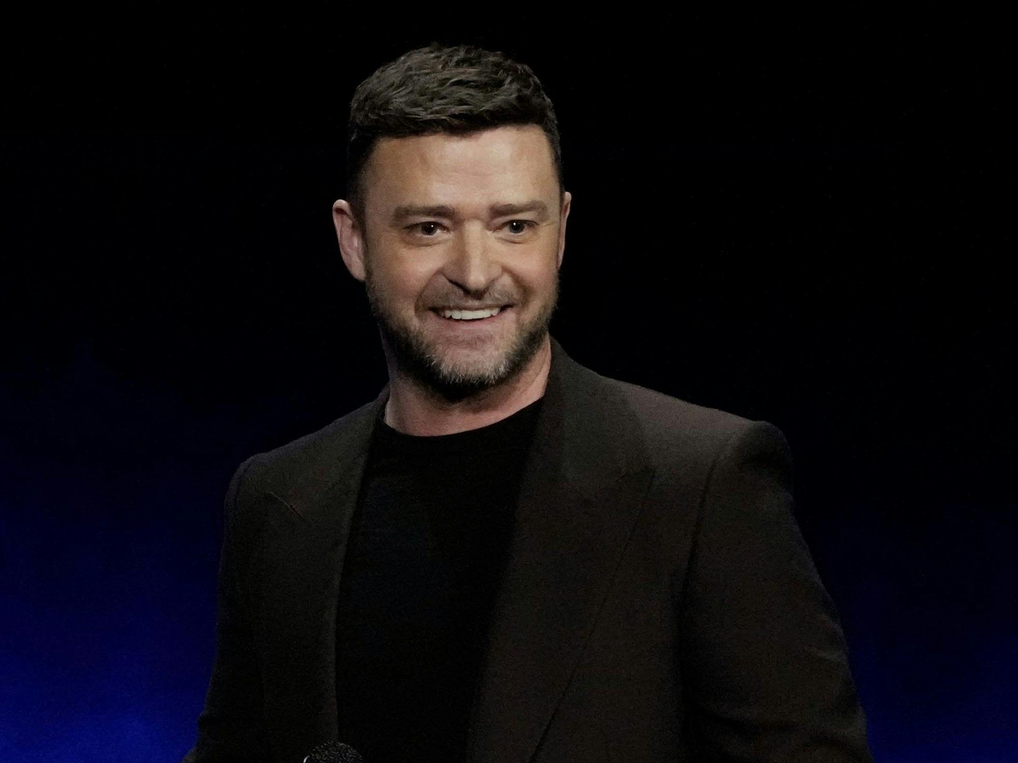 Justin Timberlake in schwarzen Klamotten auf einer Bühne, er lächelt.