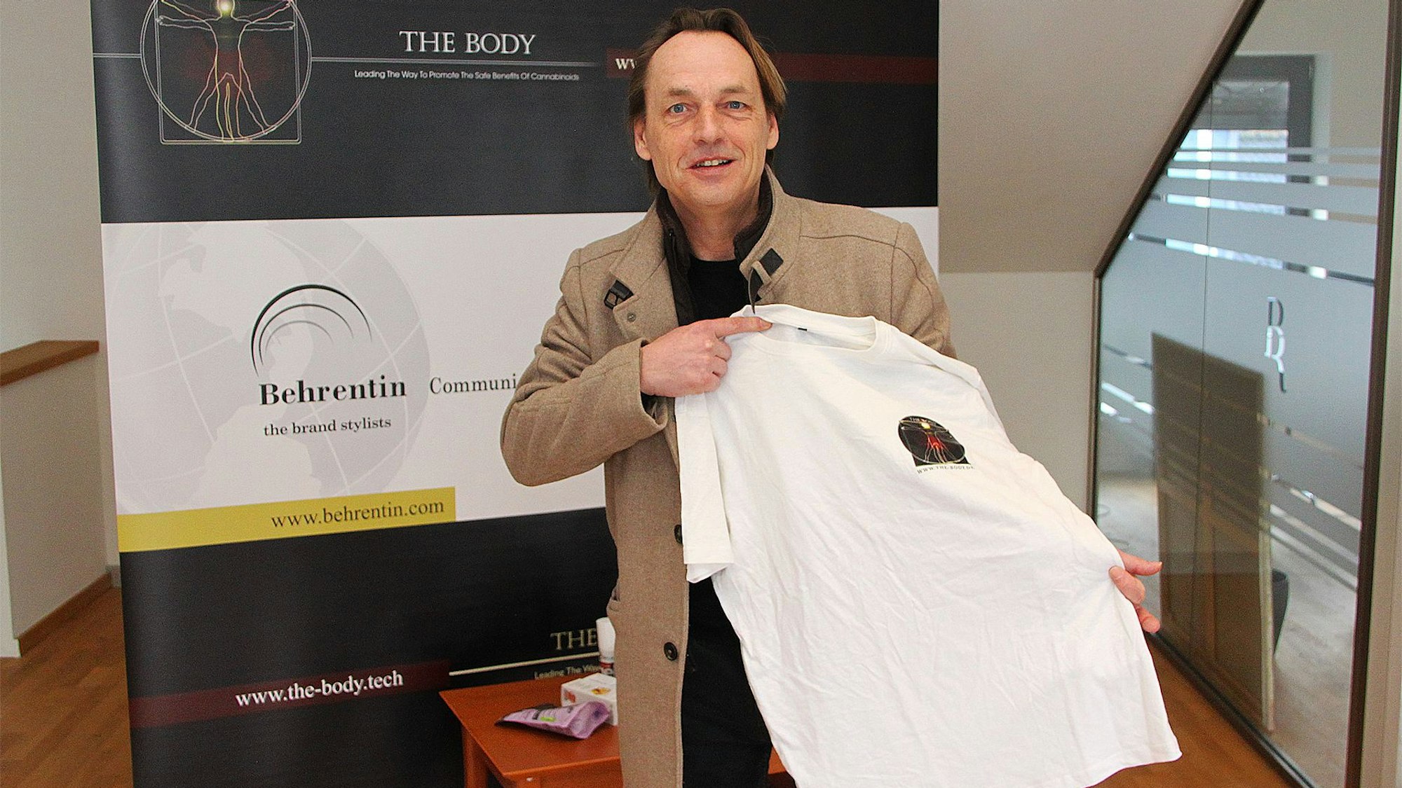 Dieter Behrentin steht in seinem Büro vor einem Werbe-Aufsteller und hält ein aus Hanf gefertigtes T-Shirt in der Hand.