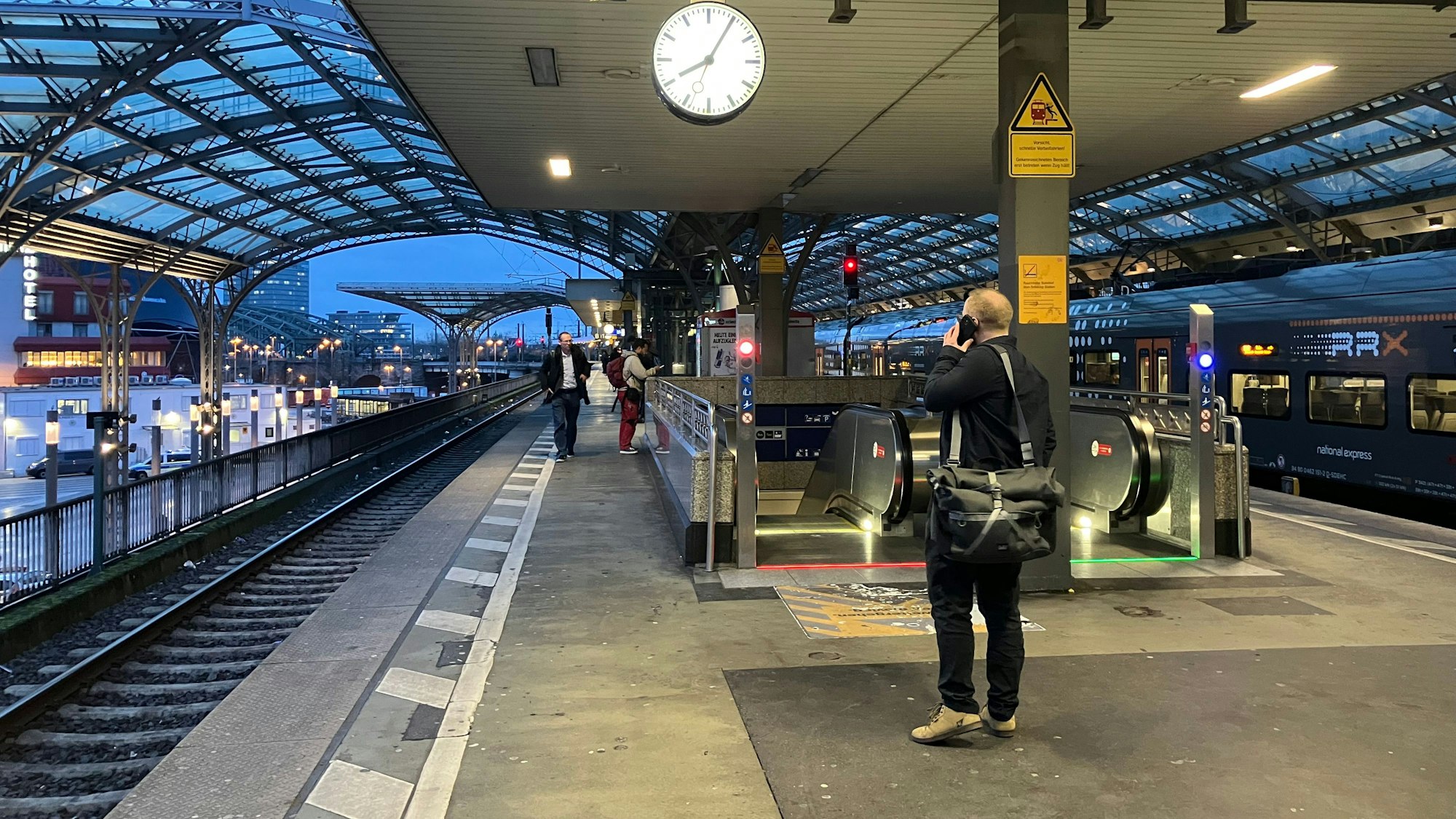 Foto von einem Bahnsteig am Kölner Hauptbahnhof, im Vordergrund ist ein Mann zu sehen, der mit dem Handy telefoniert.