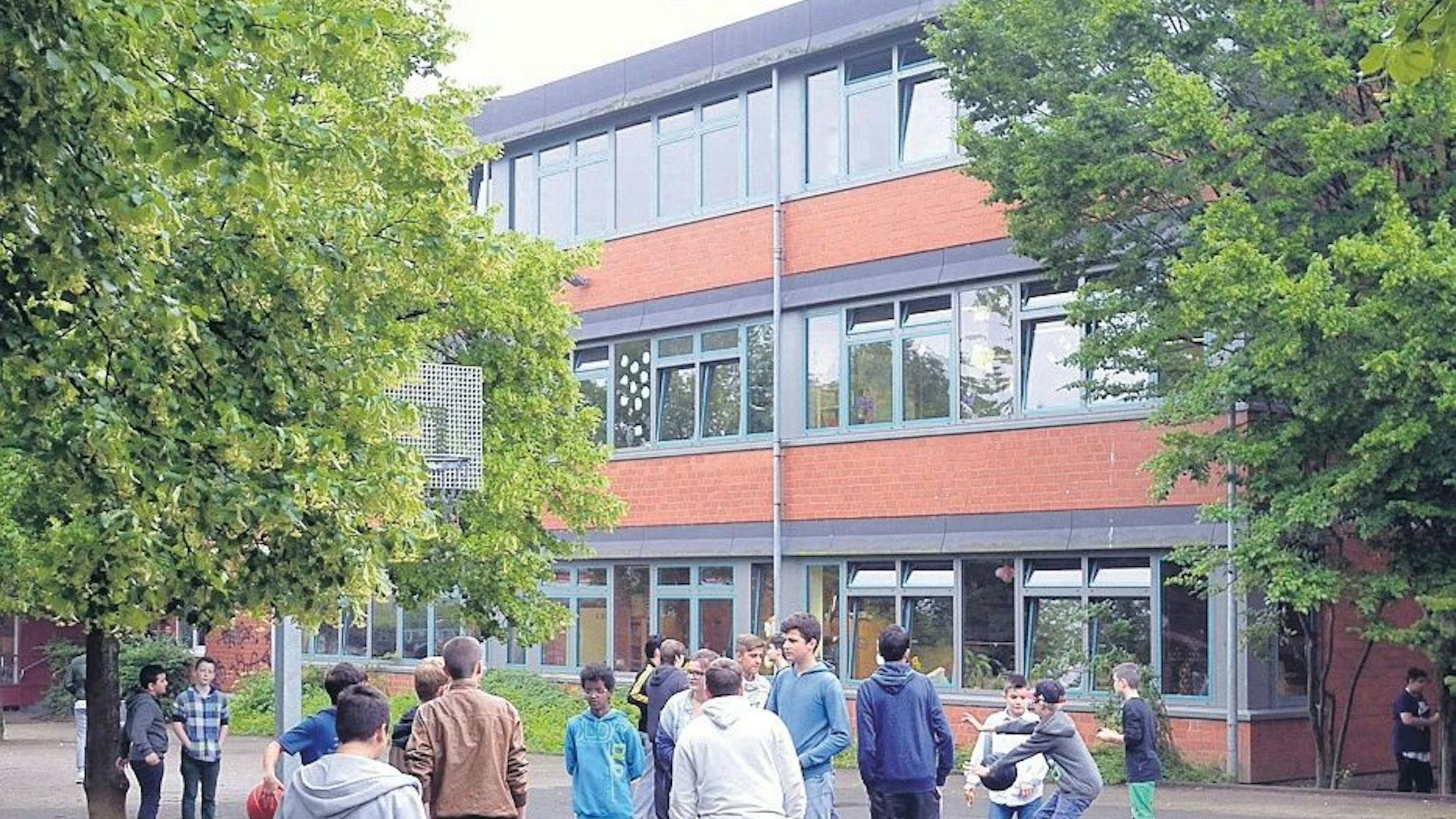 Ein Gebäude der Die Real- und Hauptschule im Kleefeld in Bergisch Gladbach ist von außen zu sehen. Auf dem Schulhof vor dem Gebäude stehen Schülerinnen und Schüler.