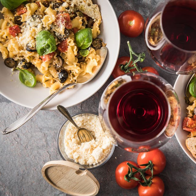 Zwei Gläser Rotwein und zwei Portionen Pasta stehen auf einem Tisch. (Symbolbild)