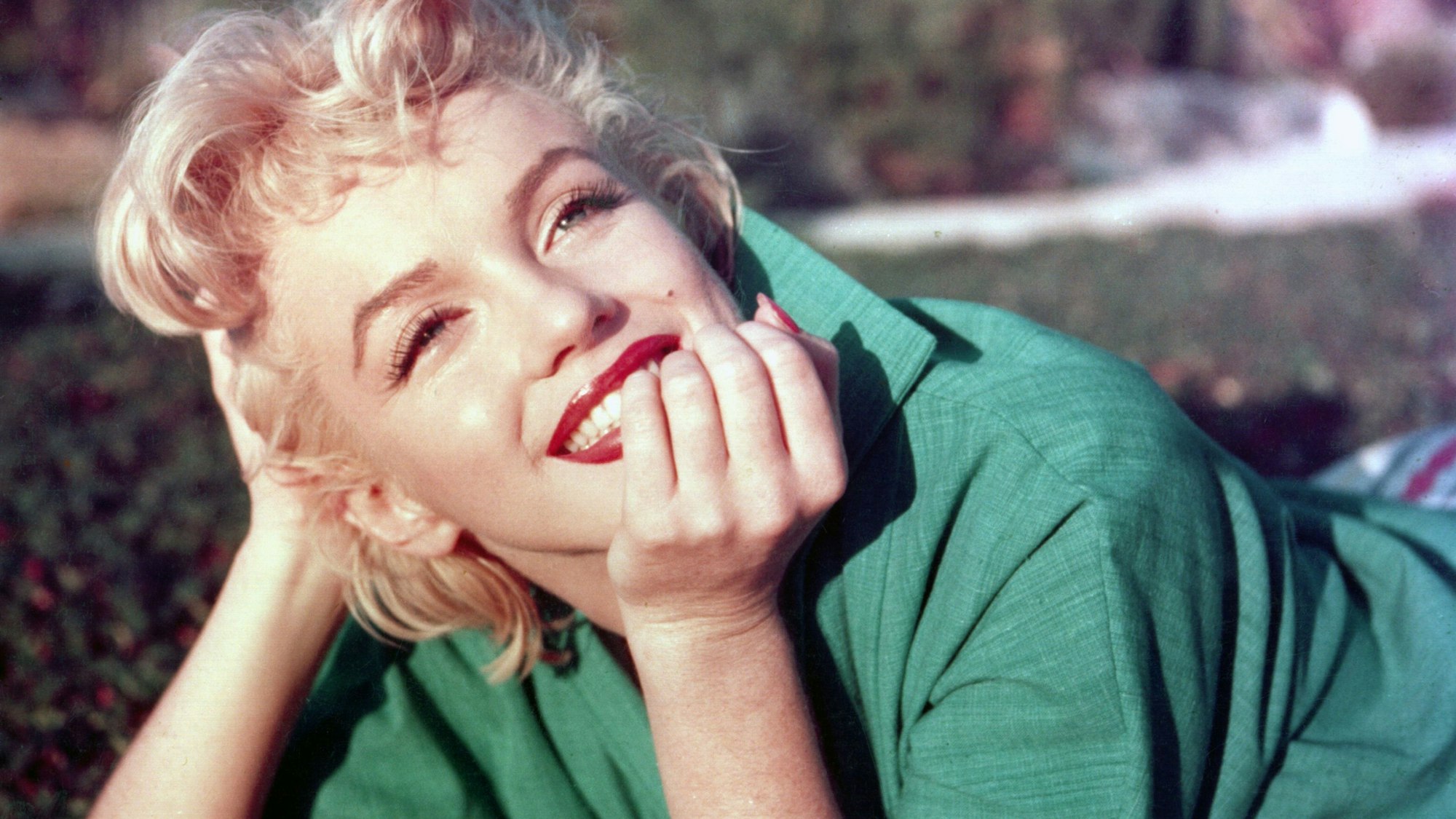Marilyn Monroe liegt auf dem Boden und lächelt.