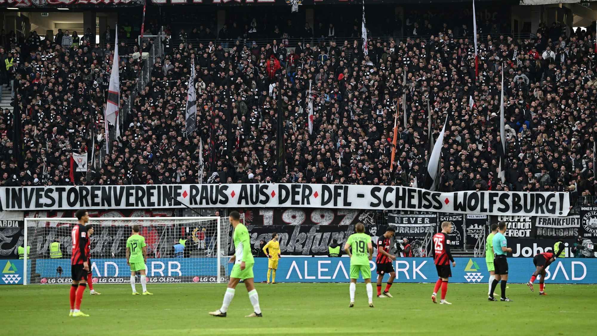 Die Frankfurter Ultras halten ein Plakat mit der Aufschrift „Investorenvereine raus aus der DFL - Scheiss Wolfsburg!“, während das Spiel unterbrochen ist.