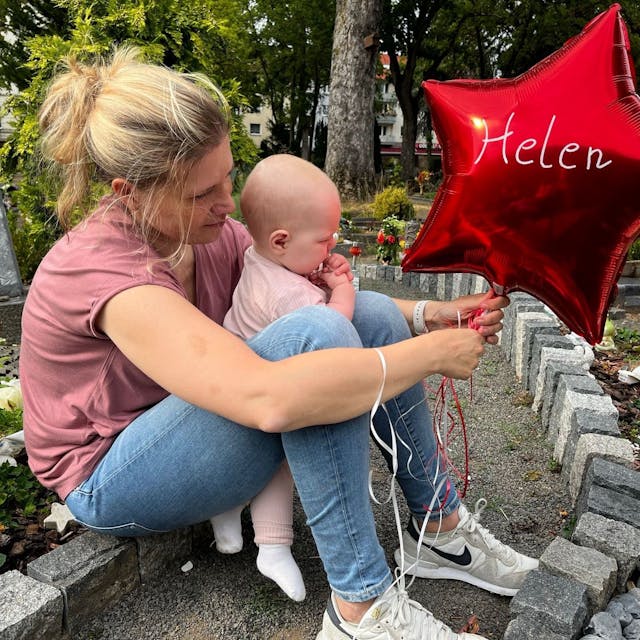 Das Bild zeigt Sarah Lenz mit Jana am Grab von Helen. Sie haben einen roten Ballon in der Hand.