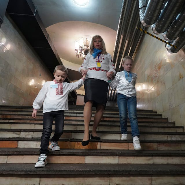 Eine Erzieherin hält die Hände von Kindern, während sie im Januar 2024 in Charkiw die Treppe zu einem unterirdischen Kindergarten in einer U-Bahn-Station hinuntergehen.