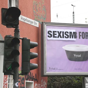 Auf einem violetten Plakat steht über einer Mehrwegschüssel „Sexism for free“. Das Wort „Sexism“ wurde nachträglich über das Plakat geklebt.