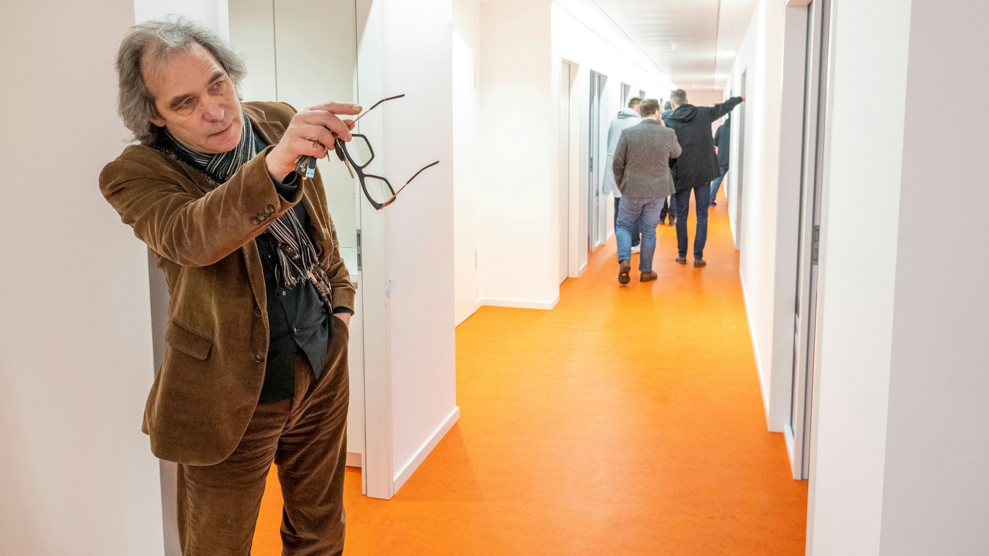 Zu sehen sind mehrere Personen in einem Flur der KHM Köln. Der Boden ist orange und die Wände und die Decke sind weiß.