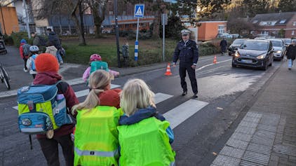 Schulkinder gehen im Beisein eines Polizisten über einen Zebrastreifen.