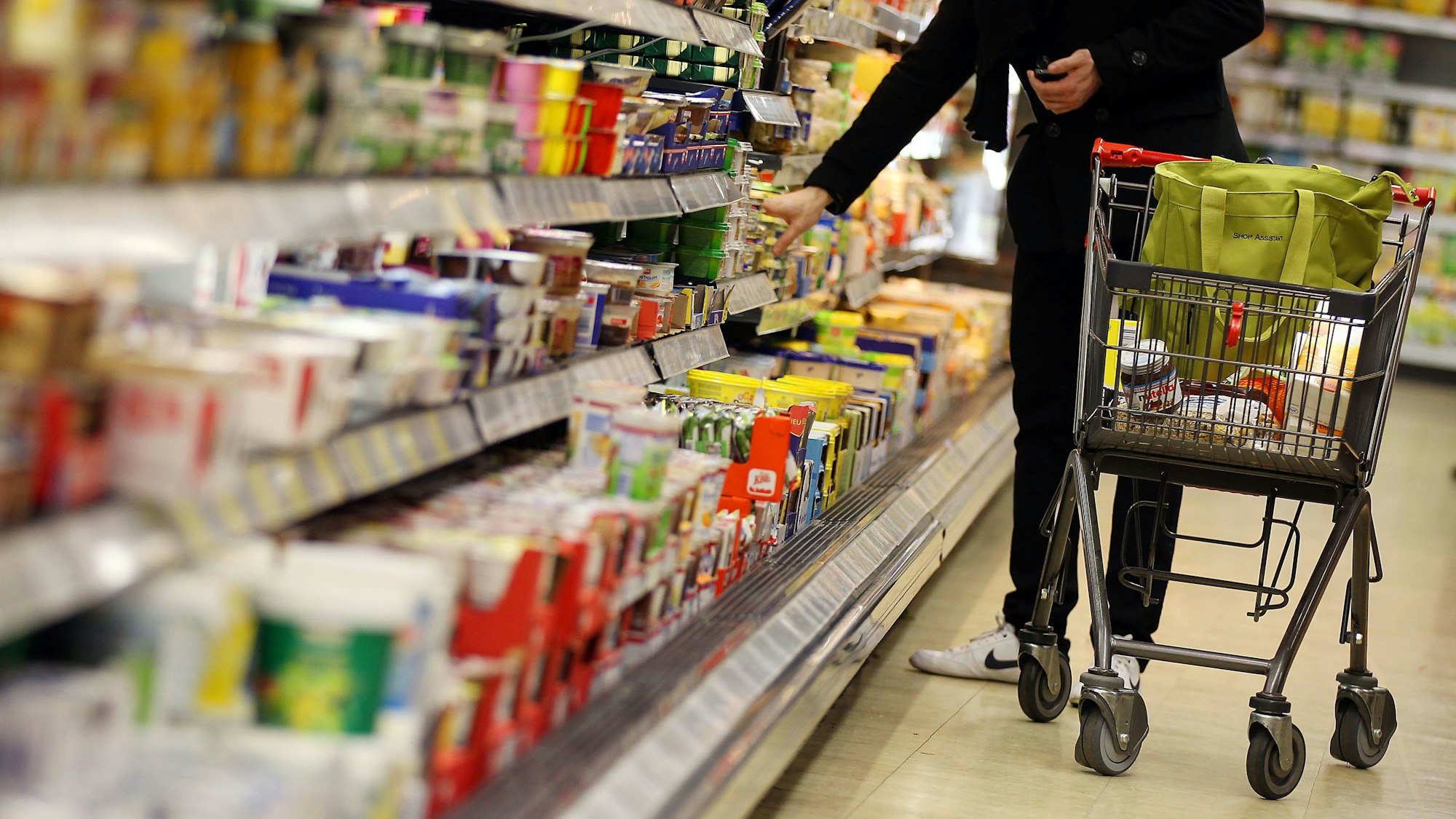 Eine Kunde steht in einem Supermarkt in Köln am Kühlregal und führt einen Einkaufswagen mit sich.