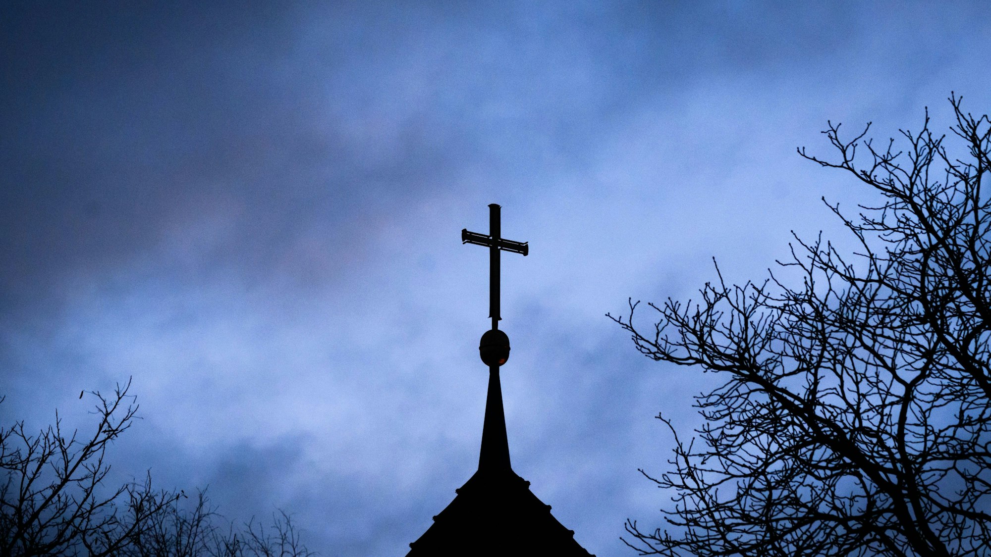 ARCHIV - 25.01.2024, Niedersachsen, Hannover: Dunkle Wolken ziehen über das Kreuz auf einer evangelischen Kirche in der Region Hannover hinweg