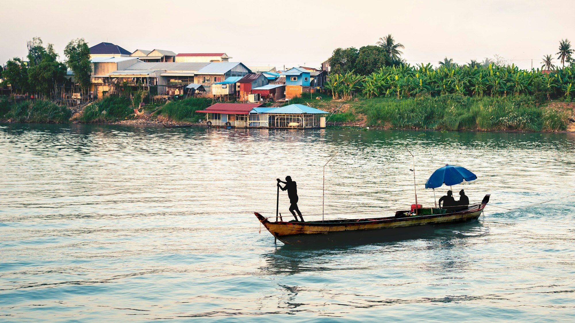 Ein Fischerboot auf dem Mekong in Kambodscha mit Dorfhäusern im Hintergrund in der Nähe von Phnom Penh.
