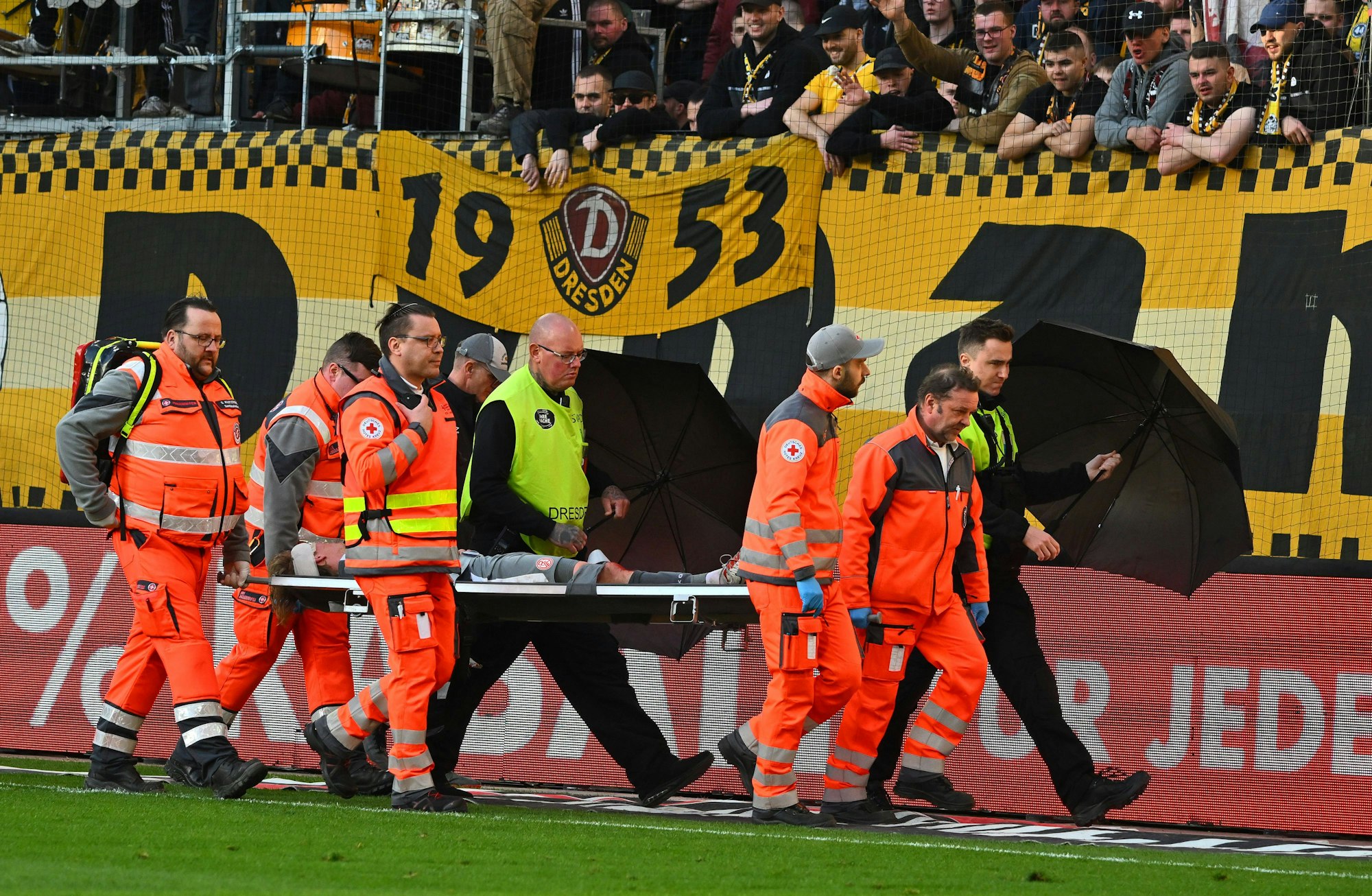 Felix Götze wird verletzt vom Platz getragen. Anhänger von Dynamo Dresden pöbeln dennoch.