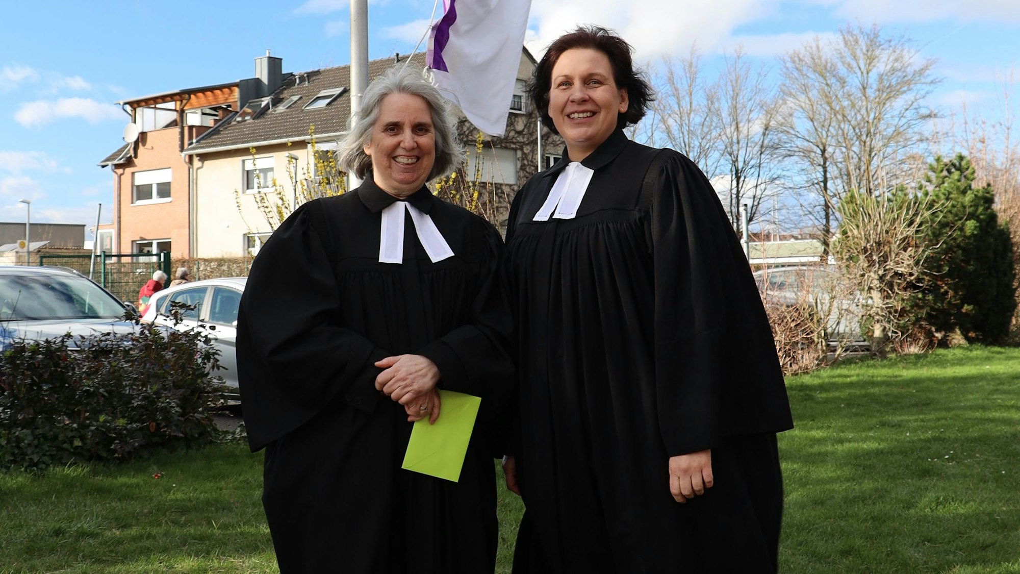 Die Pfarrerin Renate Kalteis und Superintendentin Claudia Müller-Bück stehen in ihrem schwarzen Talar auf einer Wiese.