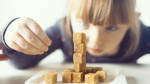 Ein kleines Mädchen sitzt an einem Tisch und stapelt Zuckerwürfel aufeinander.