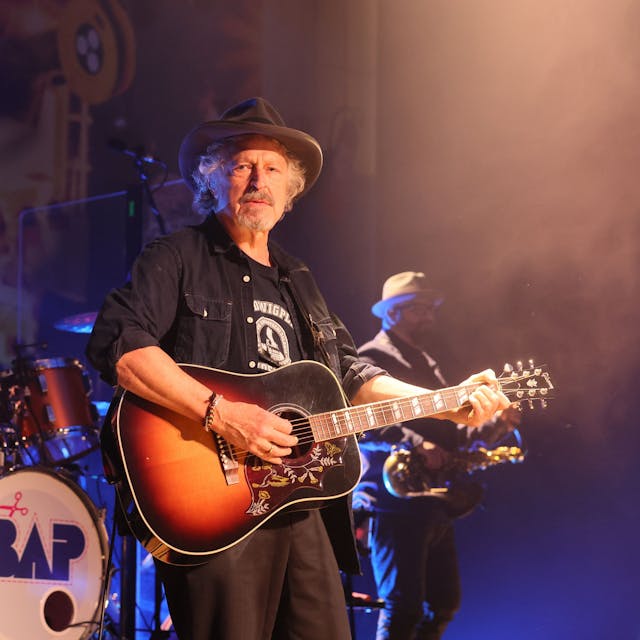Wolfgang Niedecken steht mit Gitarre auf der Bühne.