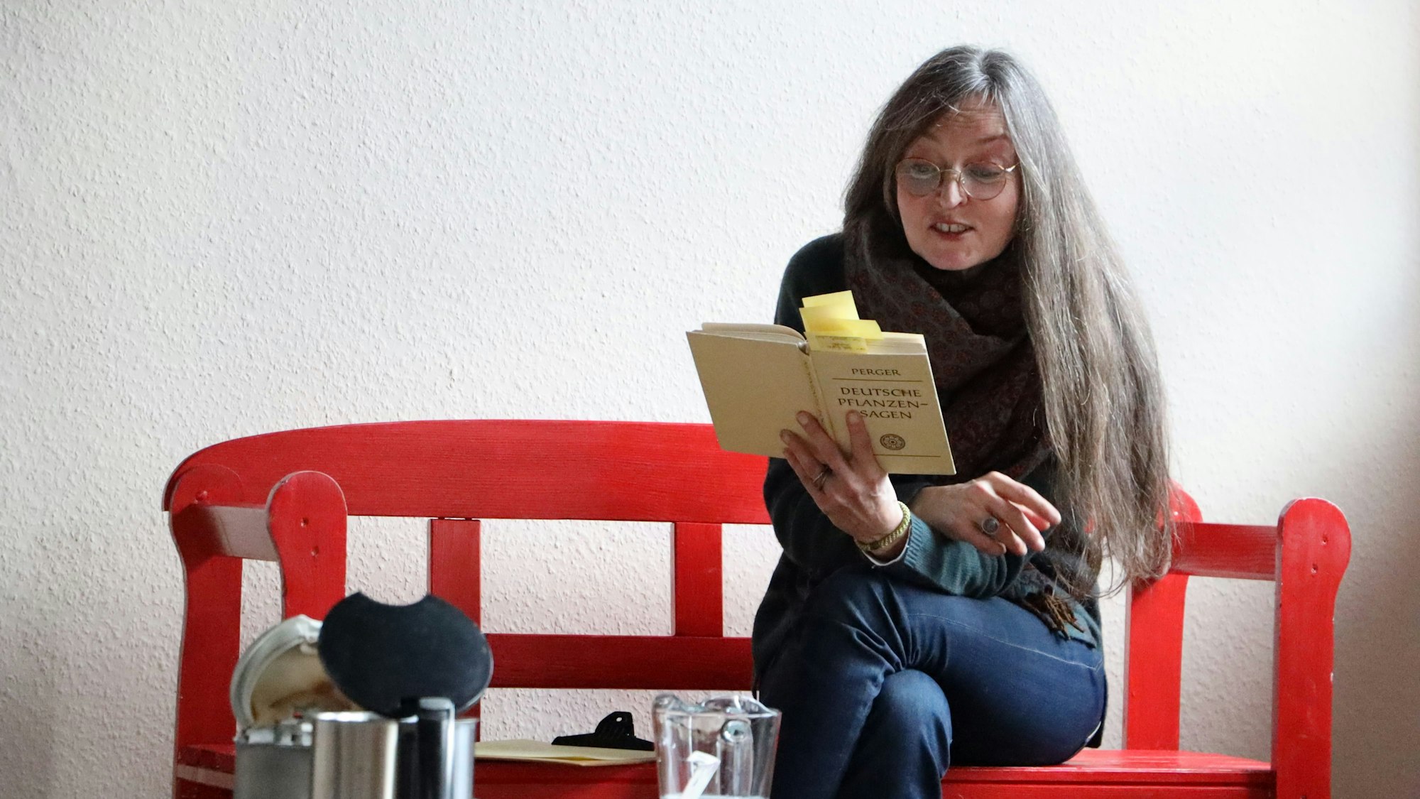 Christiane Remmert vom Kulturhaus Theater 1 sitzt auf einer roten Bank und liest aus einem Buch vor.