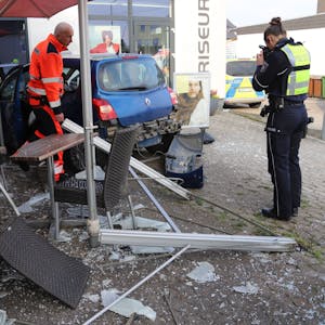 Ein Polizist fotografiert einen Kleinwagen, der in den Trümmern einer Außengastronomie steht, Glasscherben und zerstörte Möbel liegen auf dem Pflaster.