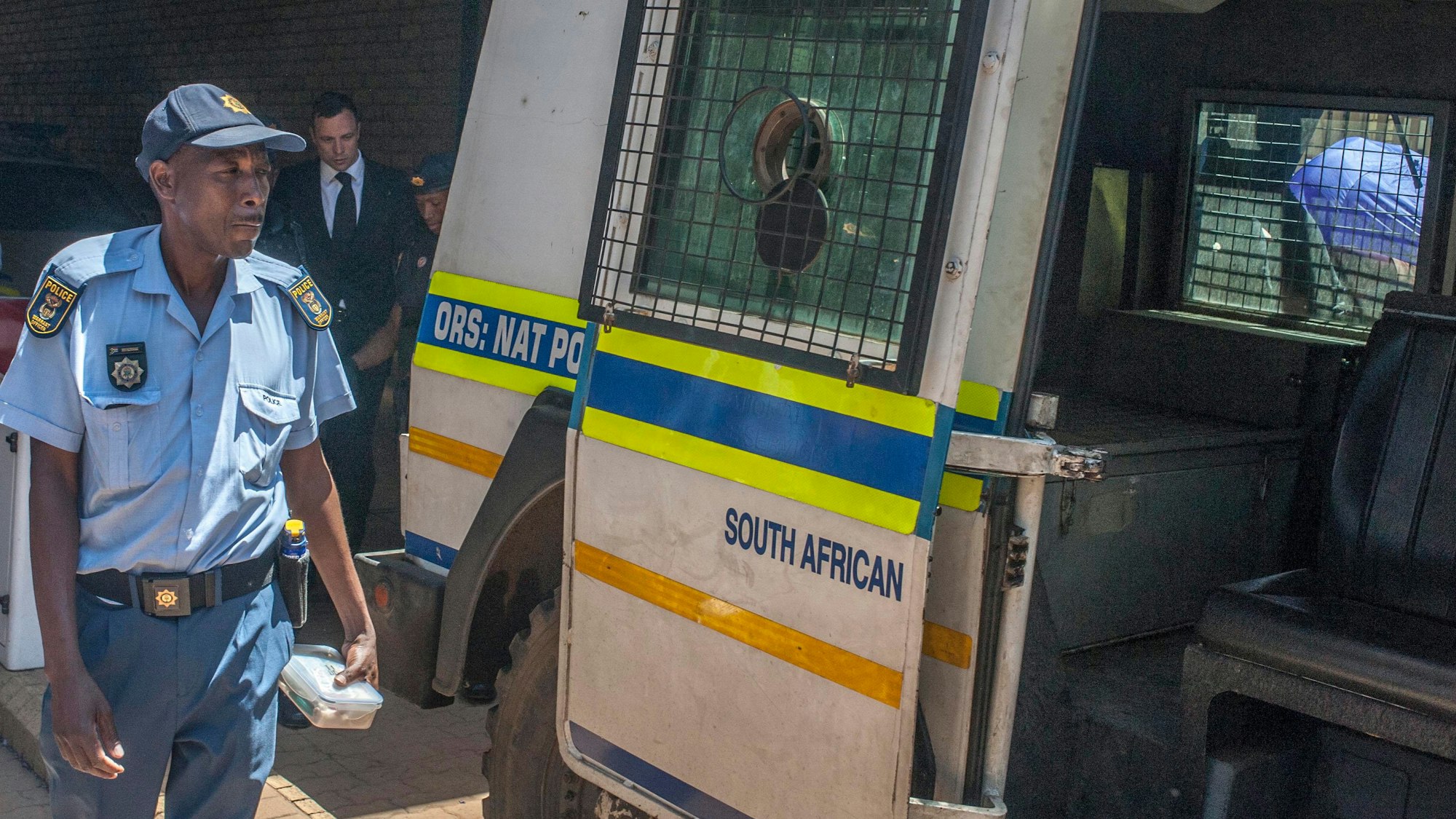 Ein Polizeibeamter in Südafrika steht vor einem Polizeiwagen.