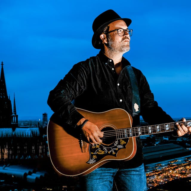 Björn Heuser steht mit Gitarre am Rheinufer