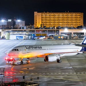 Ein Flugzeugschlepper zieht ein Flugzeug der Lufthansa auf einem Rollfeld. Mehrere Warnleuchten sind dabei angeschaltet. (Symbolbild)