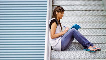 Frau sitzt auf Treppe und schreibt in ein Heft.