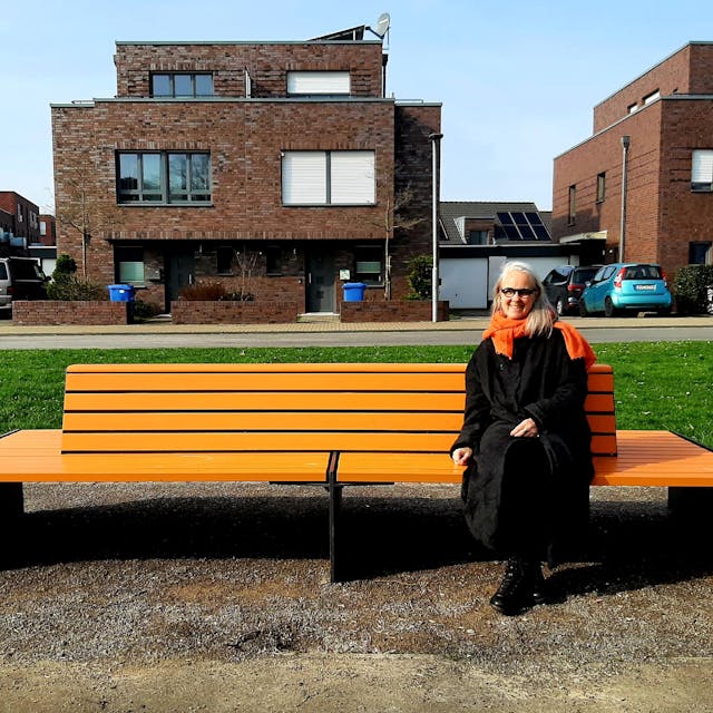 Susanne Wedewer vom Zonta-Club Leverkusen sitzt auf der vom Zonta-Club aufgestellten orangenen Bank in der Neuen Bahnstadt Opladen, auf der sie demnächst regelmäßig (bekannte) Menschen der Stadt zum Thema Frauenrechte, Gleichstellung, Sexismus, Gewalt gegen Frauen befragen will.  