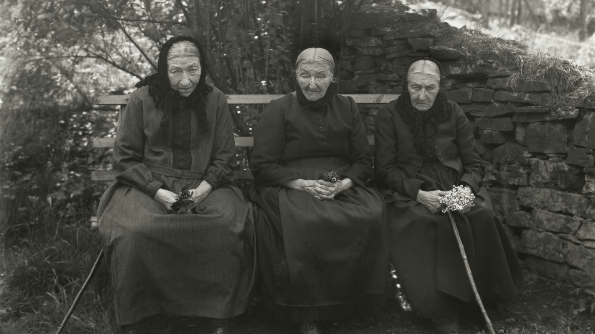 Drei greise Frauen sitzen nebeneinander auf einer Bank.