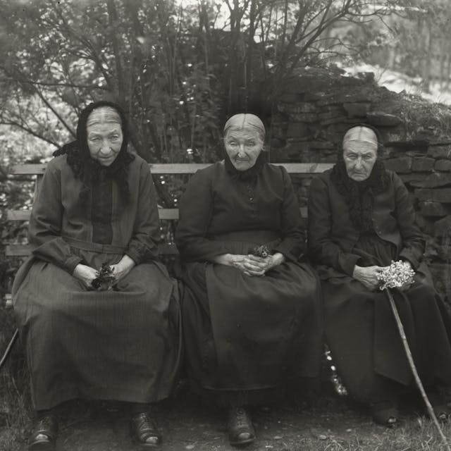 Drei greise Frauen sitzen nebeneinander auf einer Bank.