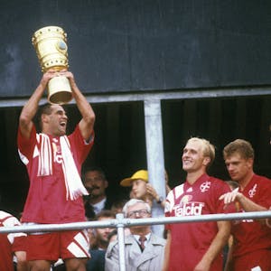Spieler von Bayer Leverkusen stehen an einer Brüstung und halten jubelnd den DFB-Pokal in die Höhe.