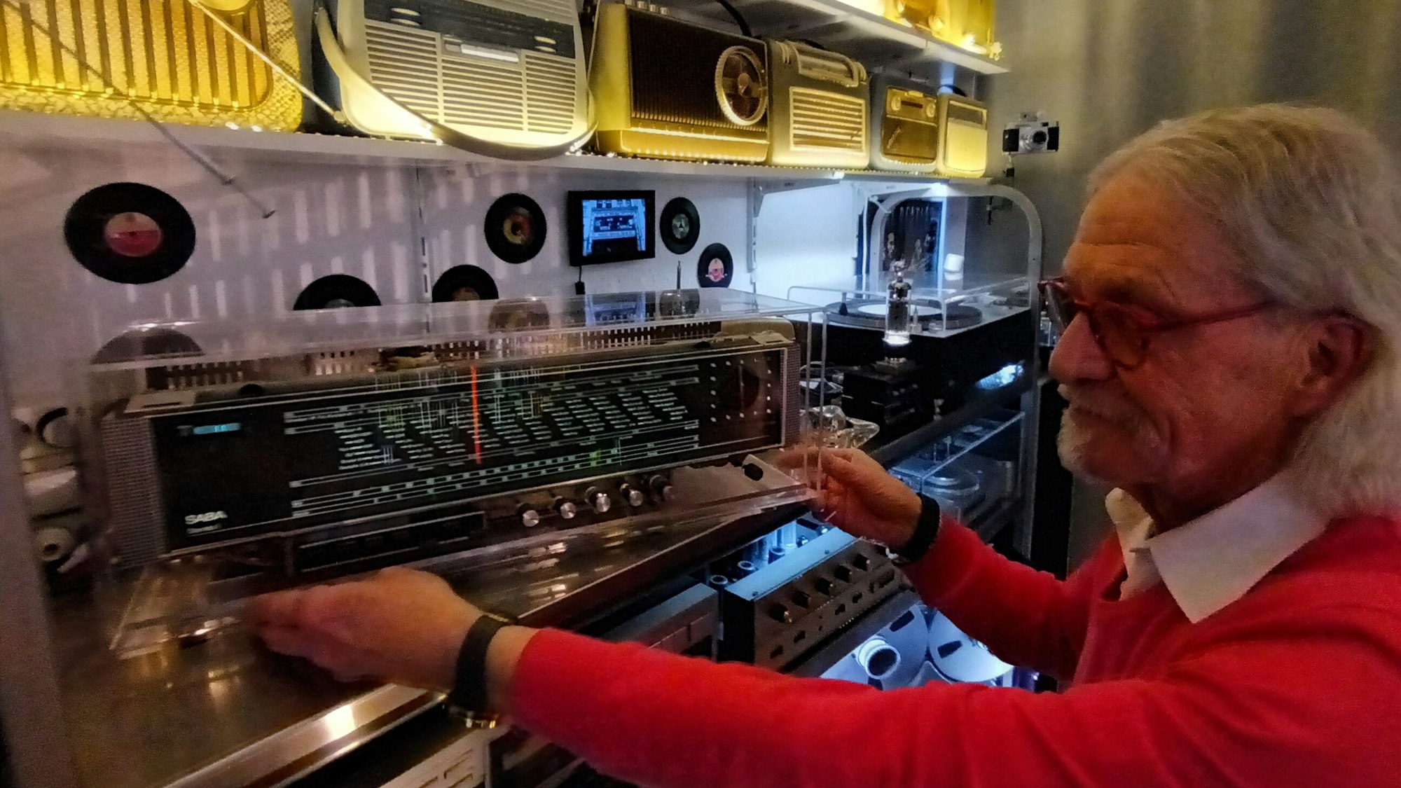 Ein Mann betrachtet ein Radio auf einem Regal voller alter Musikgeräte