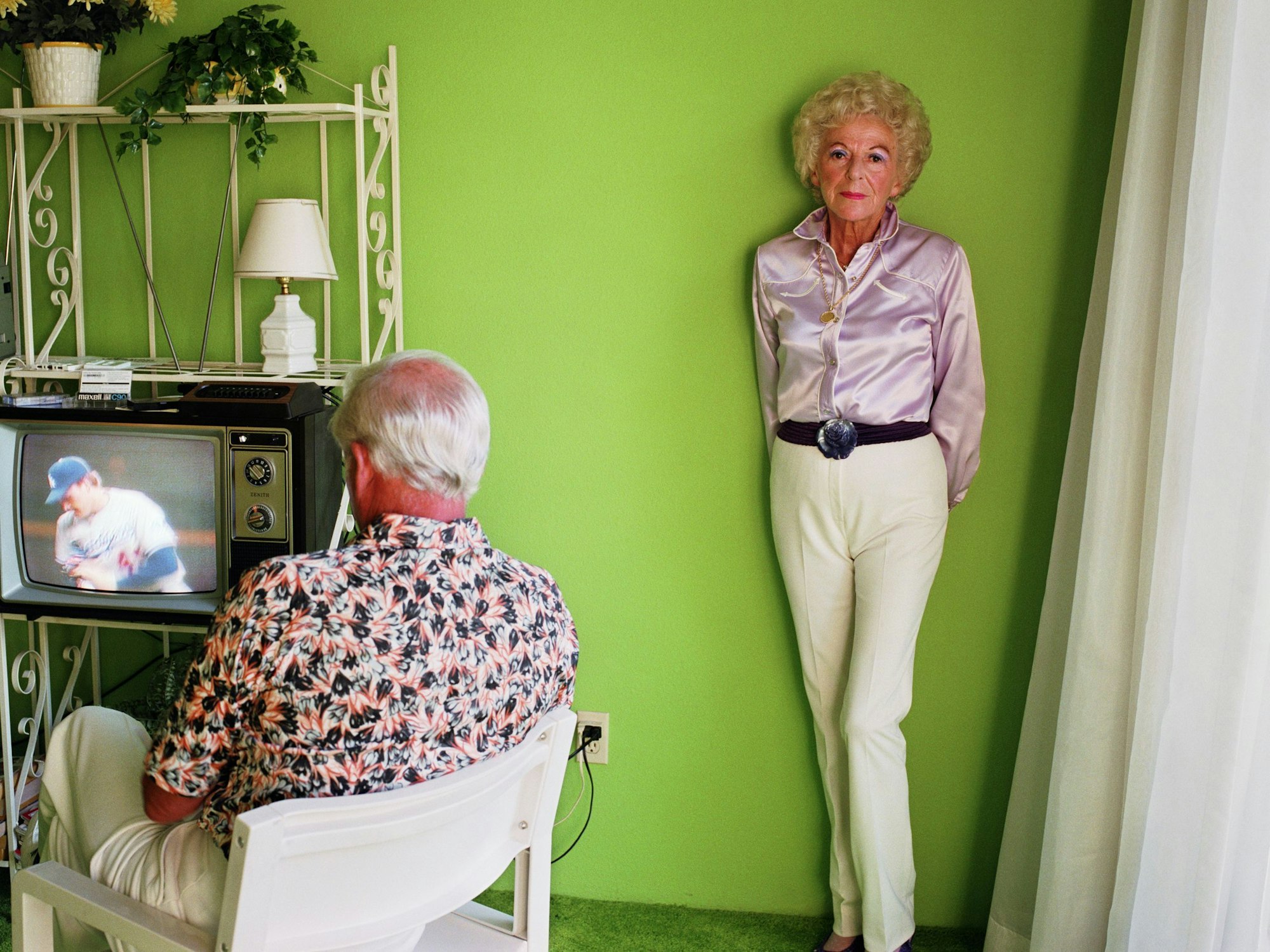 Ein Mann schaut fern, eine Frau lehnt an einer grünen Wand.