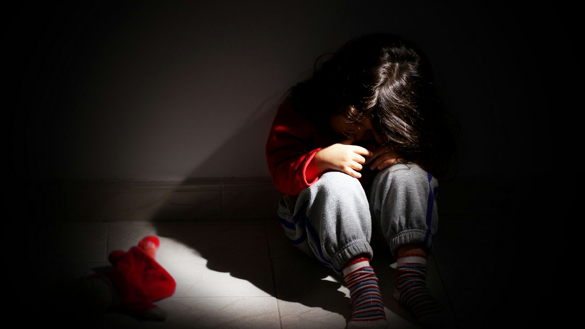 Ein kleines Mädchen sitzt zusammengekauert in einem dunklen Raum.