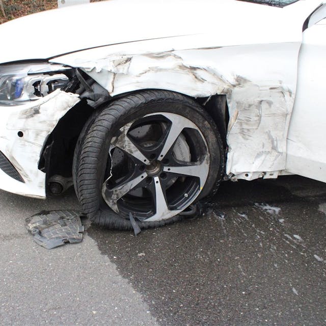 Ein weißer Mercedes hat nach einem Zusammenstoß mit einem Lkw einen starken Unfallschaden.