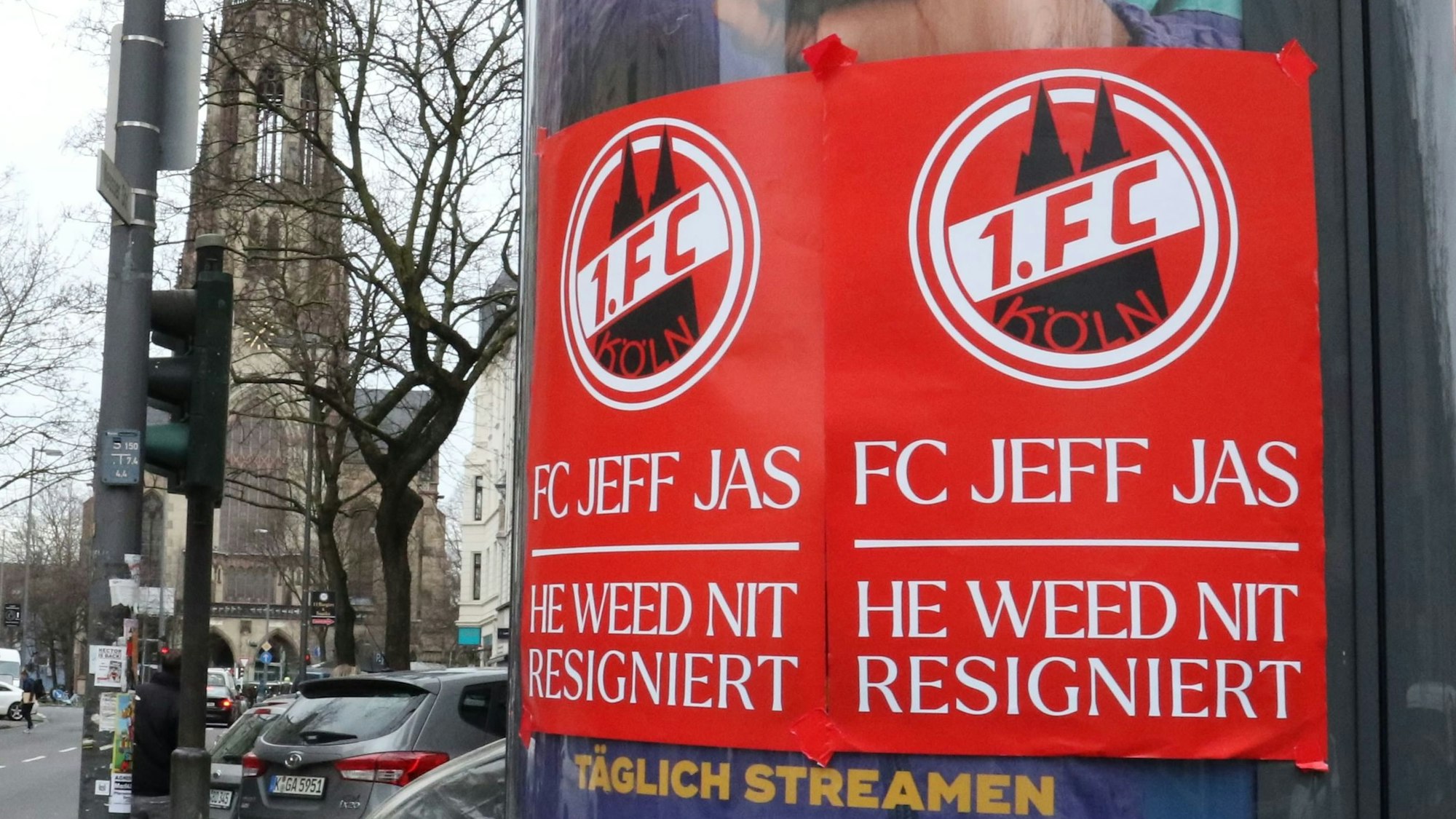 Auf einer Litfaßsäule kleben rote Plakate des 1. FC Köln mit der Aufschrift: „FC Jeff Jas – He weed nit resigniert“.