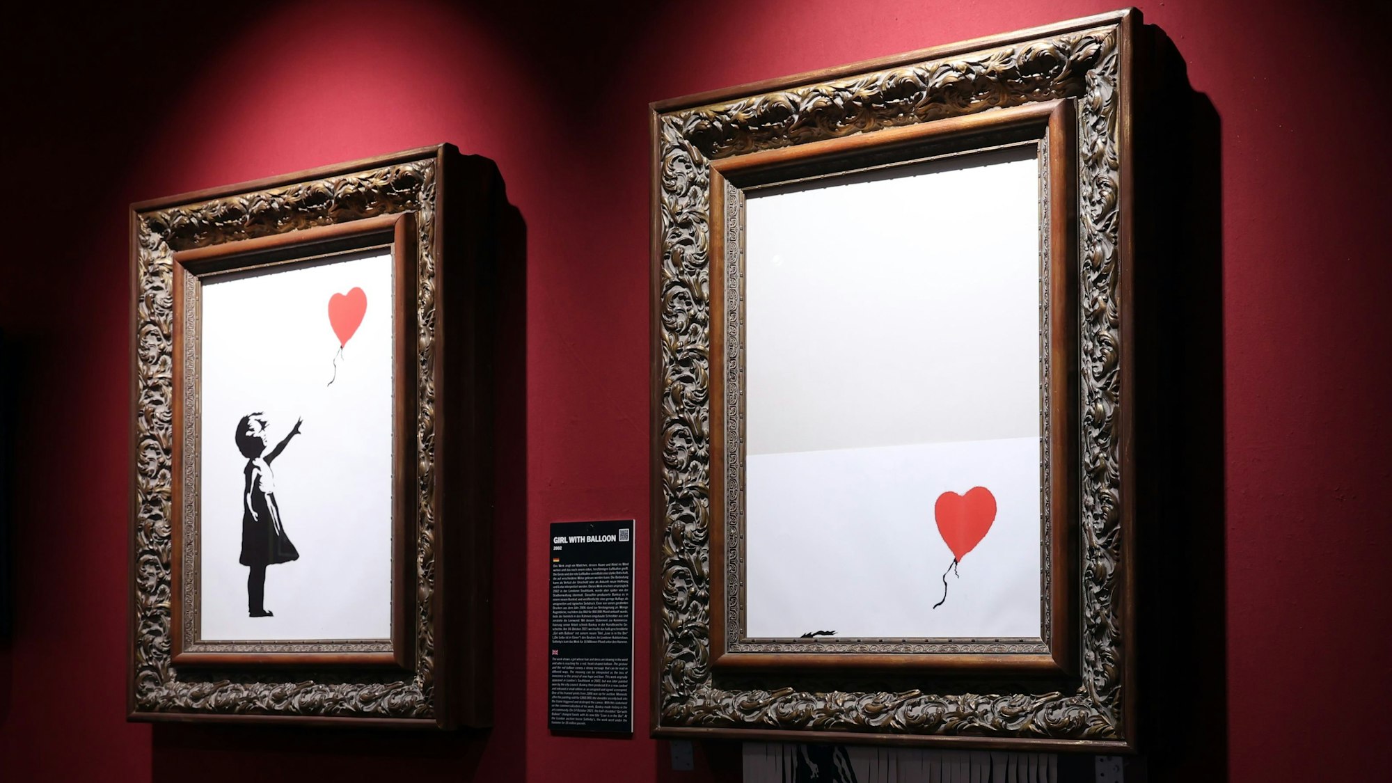 Zwei Bilder von Banksy hängen an einer roten Wand.