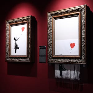 Zwei Bilder von Banksy hängen an einer roten Wand.&nbsp;