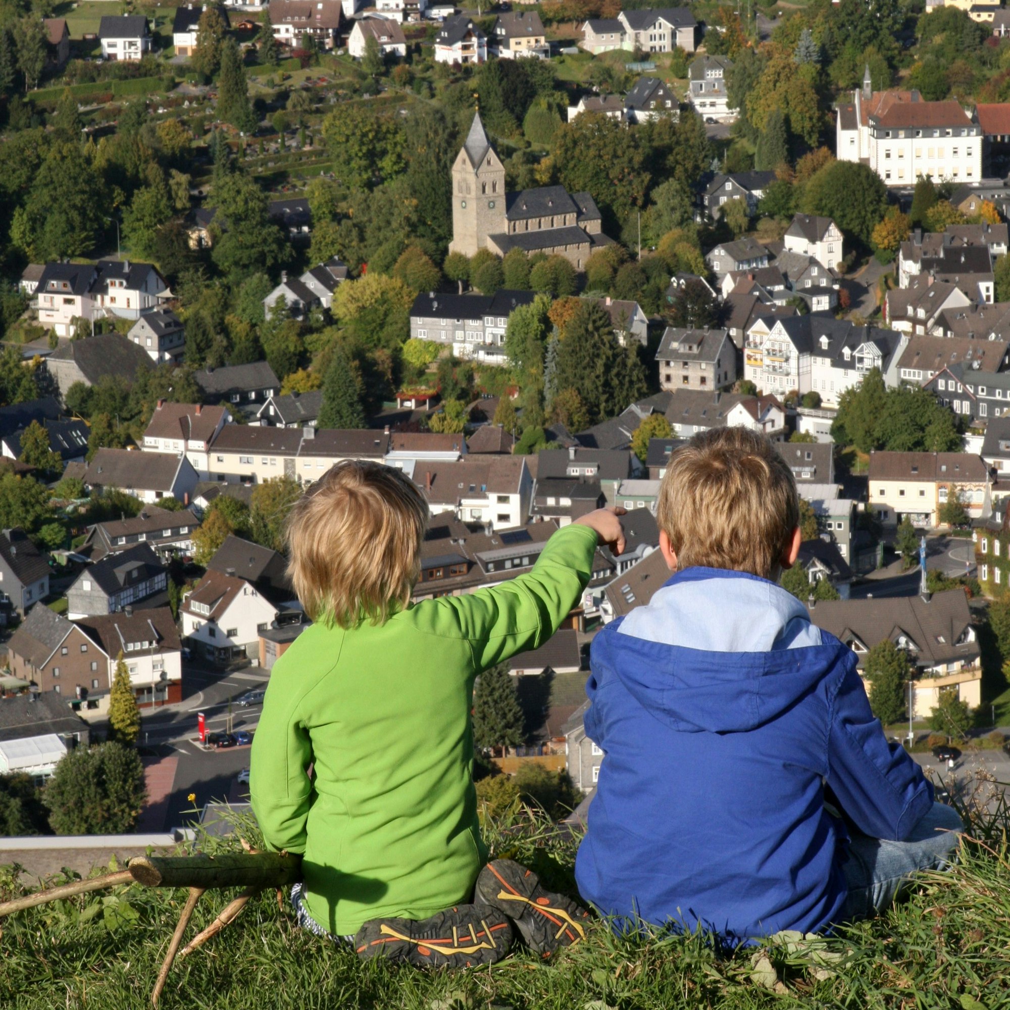 Zwei Kinder sitzen auf einer Wiese auf der Jähhardt und blicken hinunter auf den Ort Morsbach.