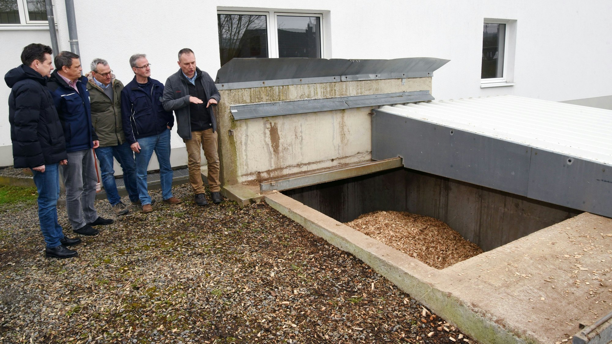 Fünf Männer stehen vor dem offenen Bunker einer Holzhackschnitzelheizung.