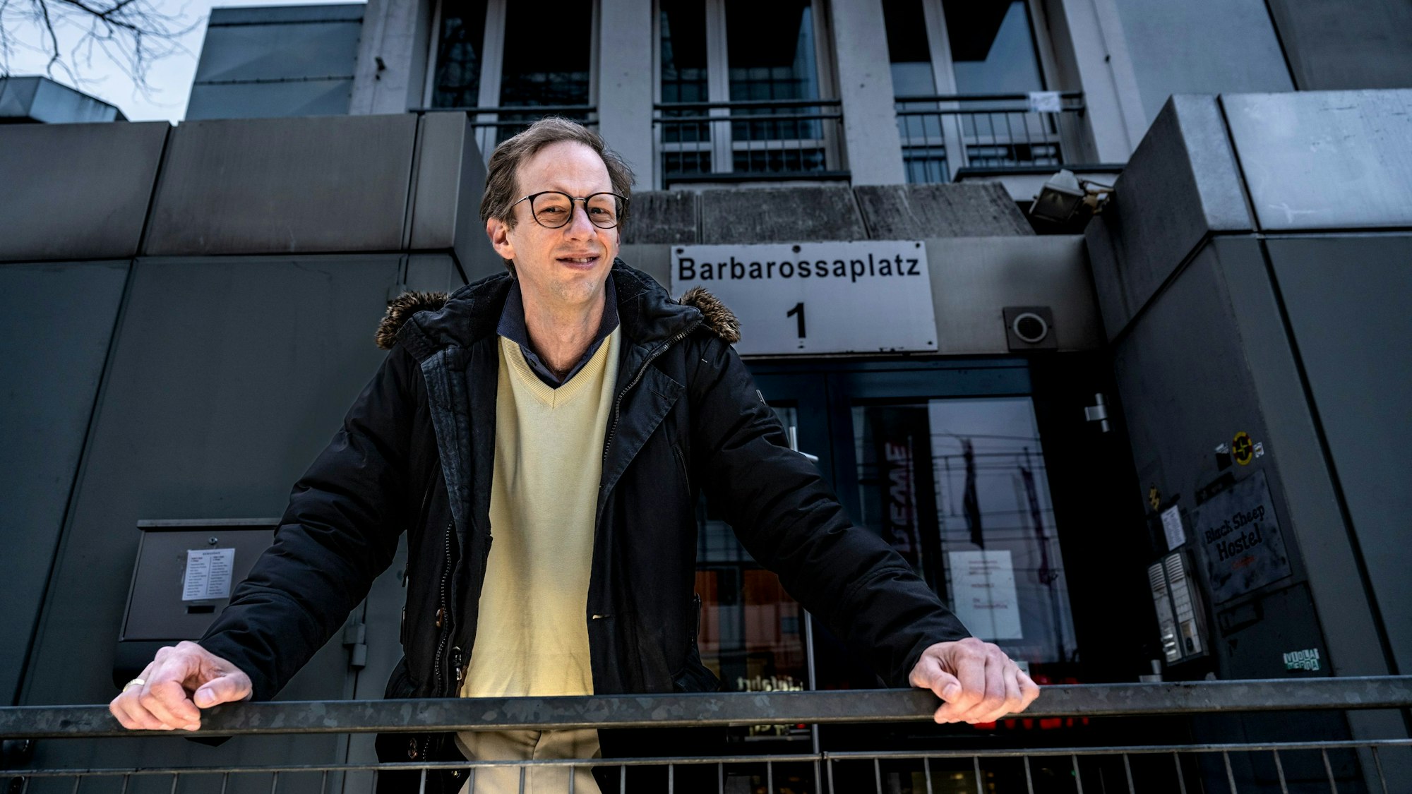 Regisseur Malte Wirtz stützt sich vor dem Haus am Barbarossaplatz 1 auf einen Zaun.