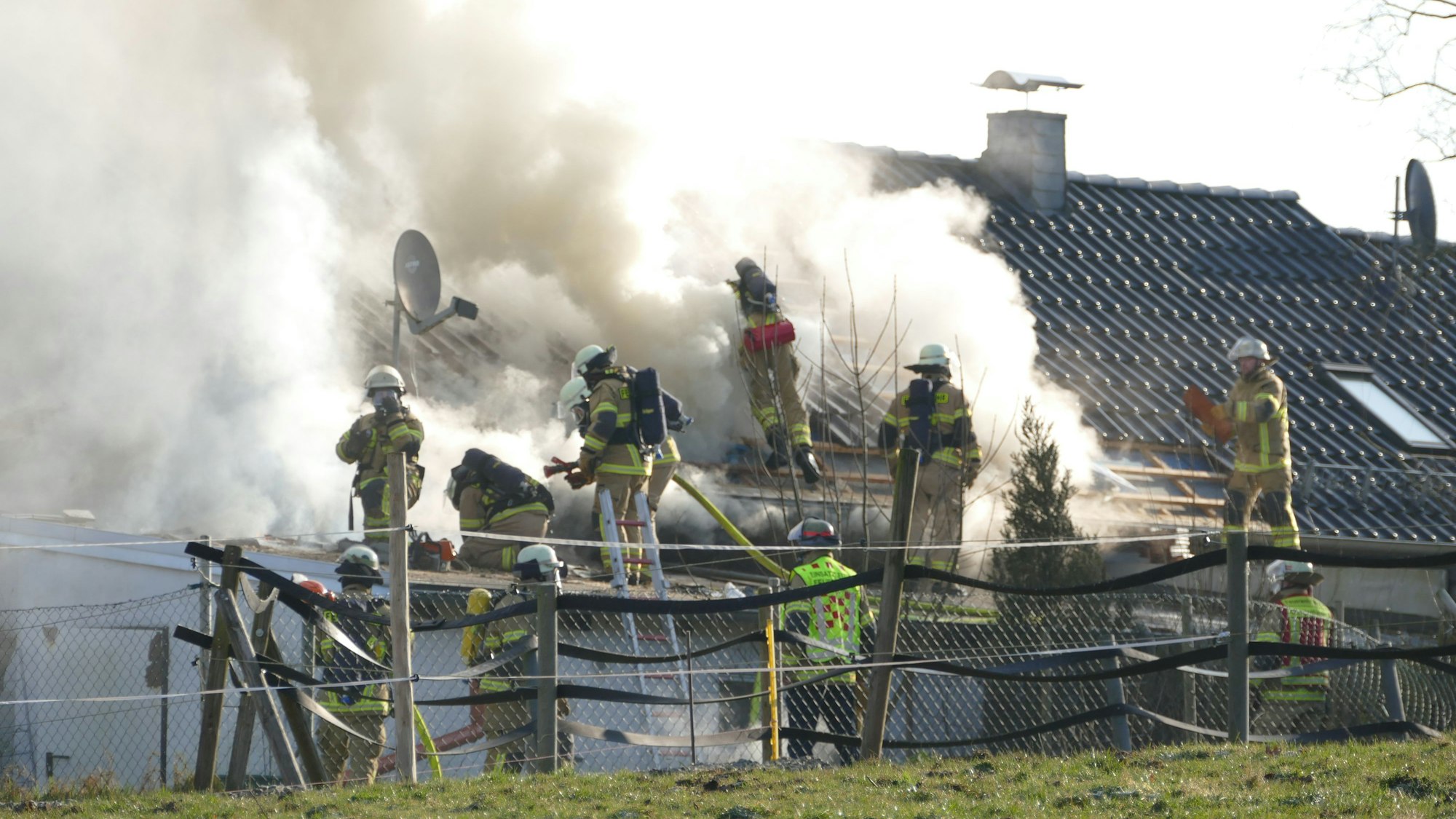Feuerwehrleute löschen ein brennendes Gebäude. Es steigen Rauch und Dampf auf.