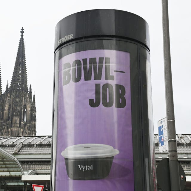 Plakate auf einer Litfaßsäule mit dem Kölner Dom im Hintergrund: Das Kölner Unternehmen Vytal warb mit dem Kunstwort „Bowljob“ für seine Mehrwegbehälter, auf die nicht direkt Pfand gezahlt werden muss.