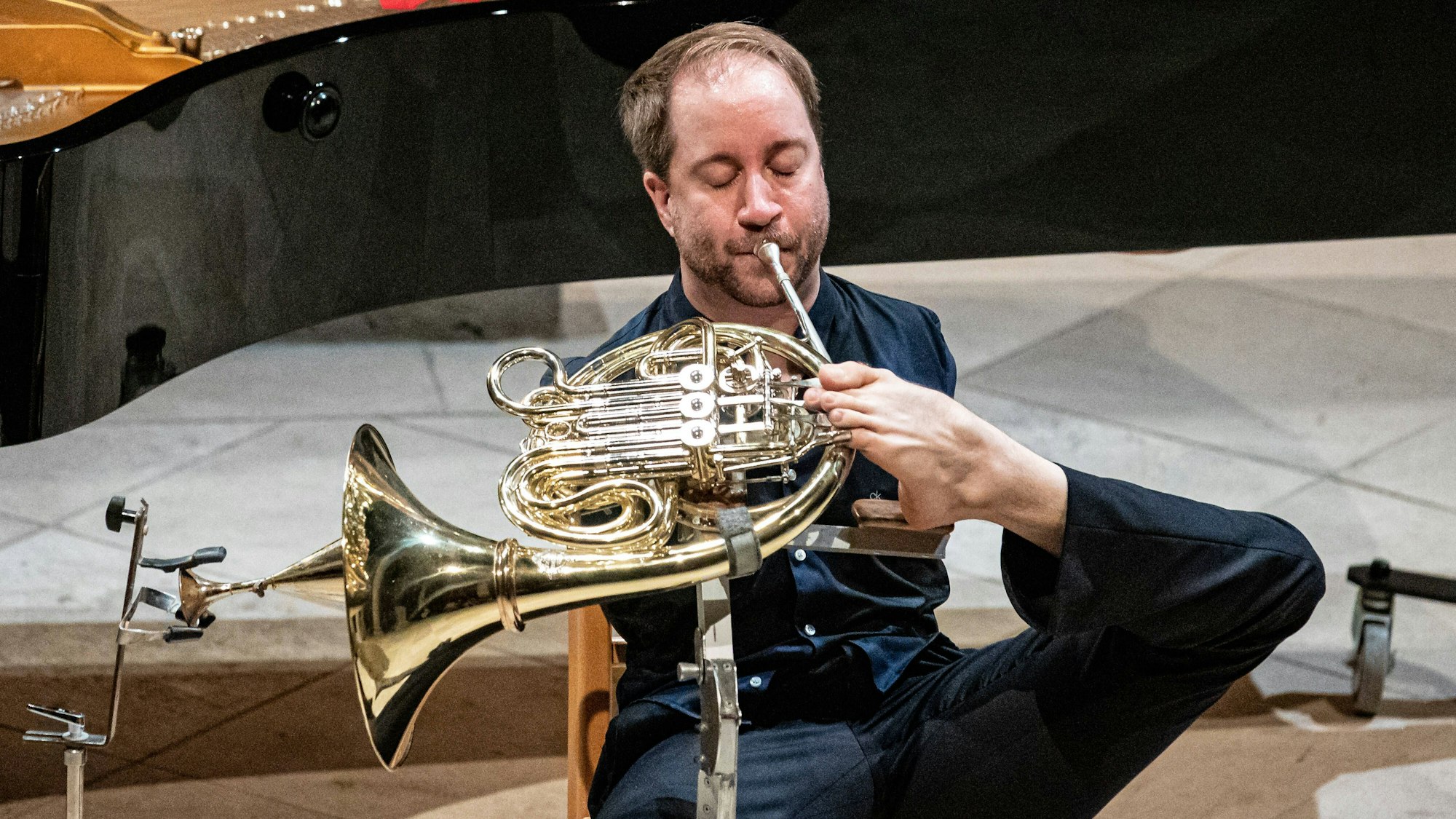 Auf dem Bild ist der Hornist Felix Klieser zu sehen, der sein Horn mit den Zehen spielt.