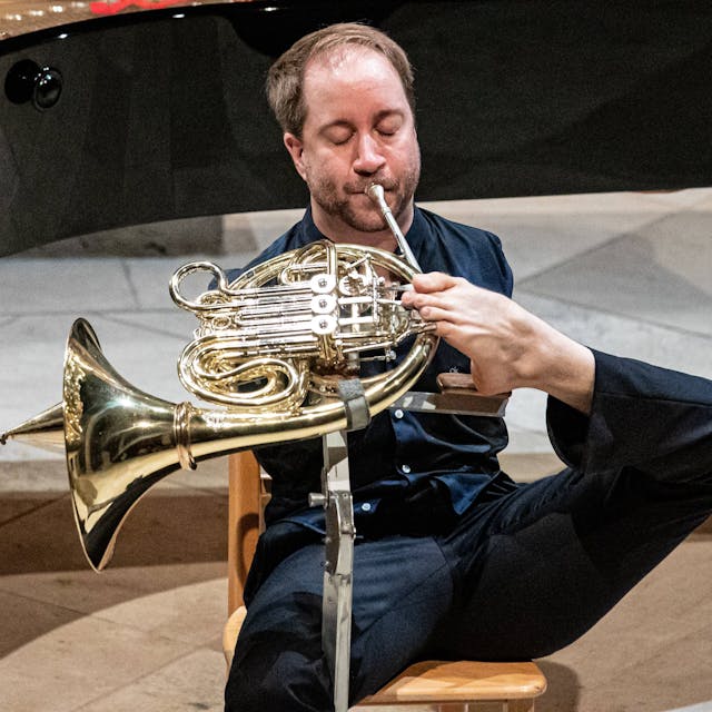 Auf dem Bild ist der Hornist Felix Klieser zu sehen, der sein Horn mit den Zehen spielt.