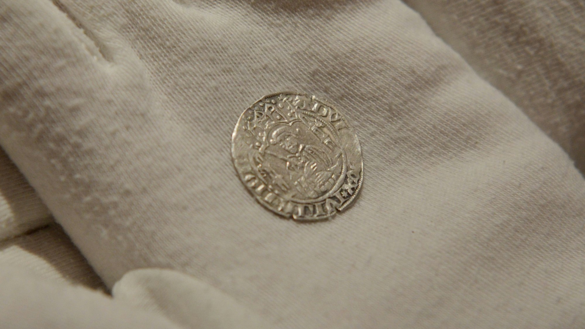 Auf einem Handschuh liegt eine der beiden Münzen mit dem Porträt des Herzogs Adolf VII. von Jülich-Berg.