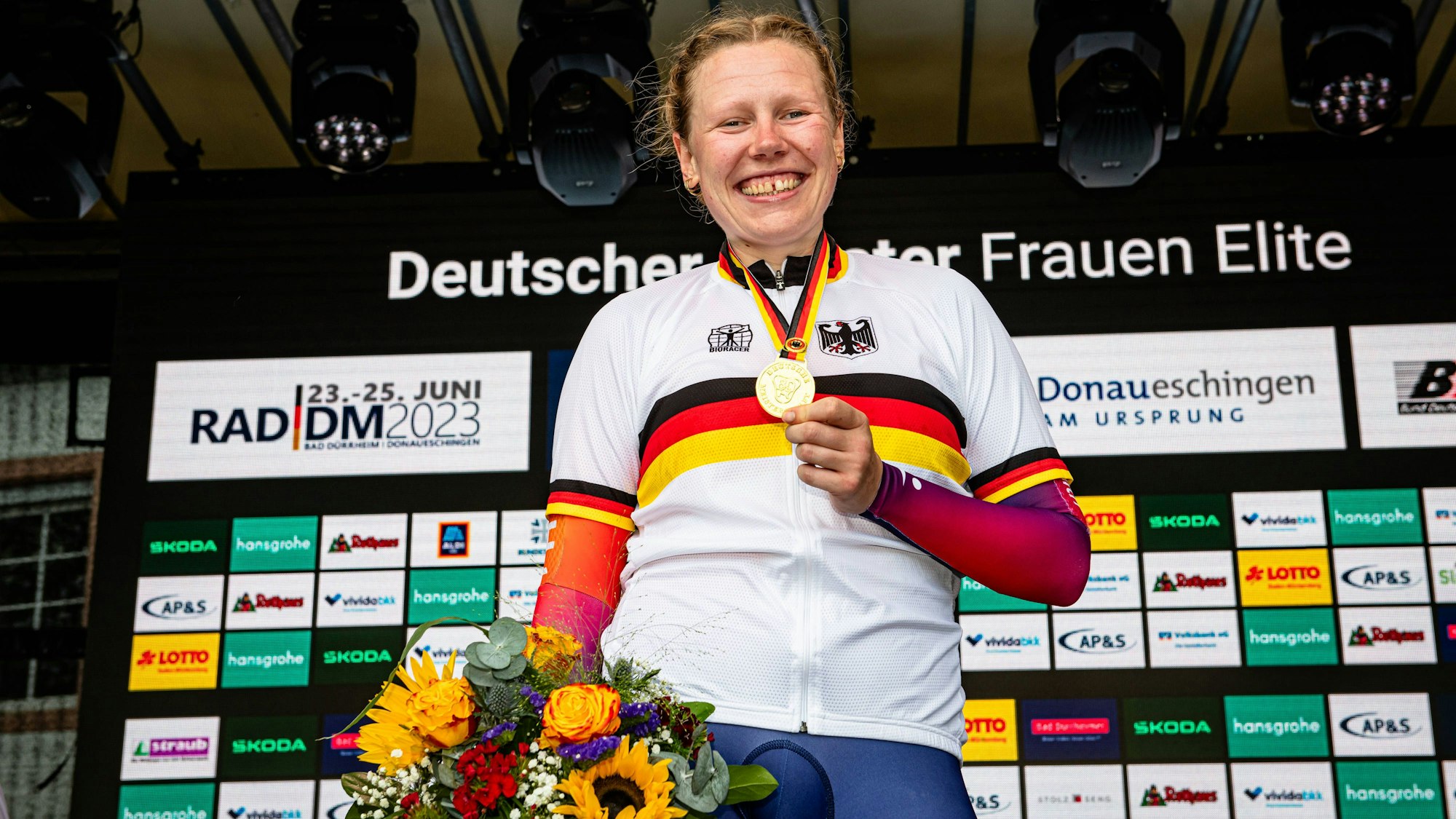 Mieke Kröger hält bei einer Siegerehrung ihre Goldmedaille in die Luft und lächelt.