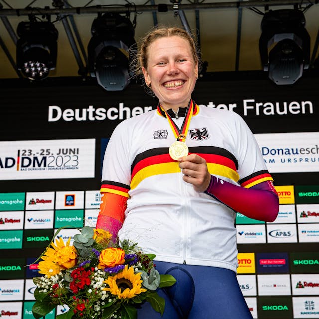 Mieke Kröger hält bei einer Siegerehrung ihre Goldmedaille in die Luft und lächelt.